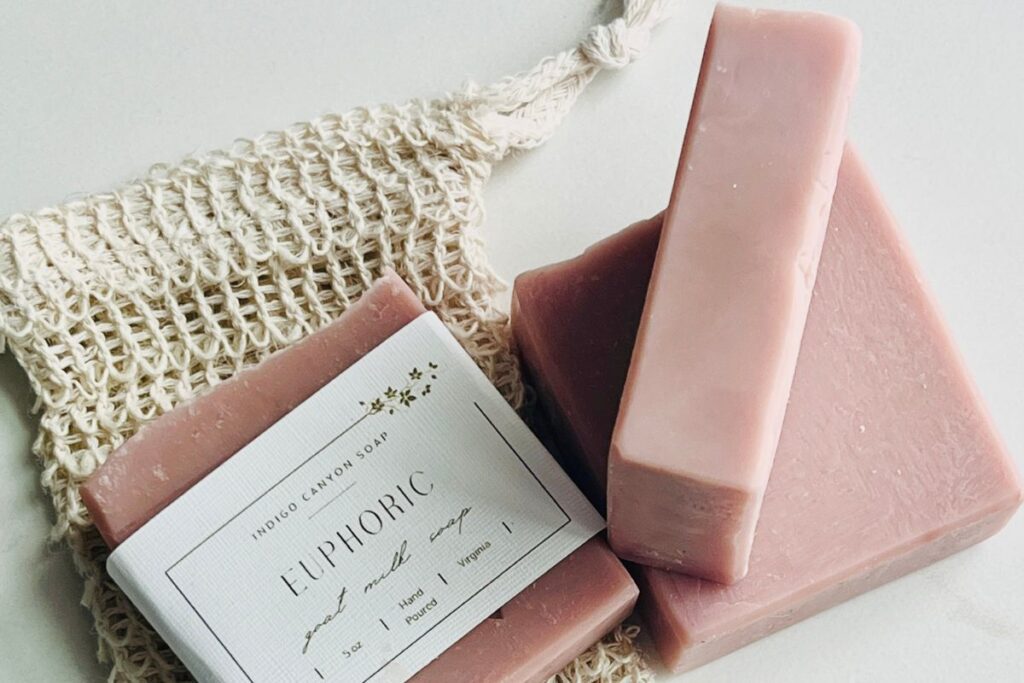 Handmade pink soaps and soap saver bag scattered on a white surface.