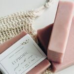 Handmade pink soaps and soap saver bag scattered on a white surface.