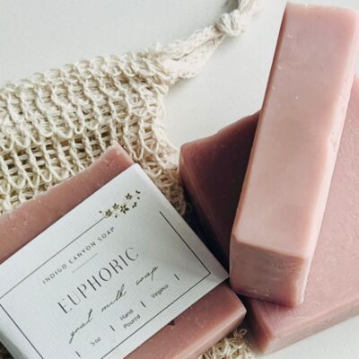 Handmade pink soaps and soap saver bag scattered on a white surface.