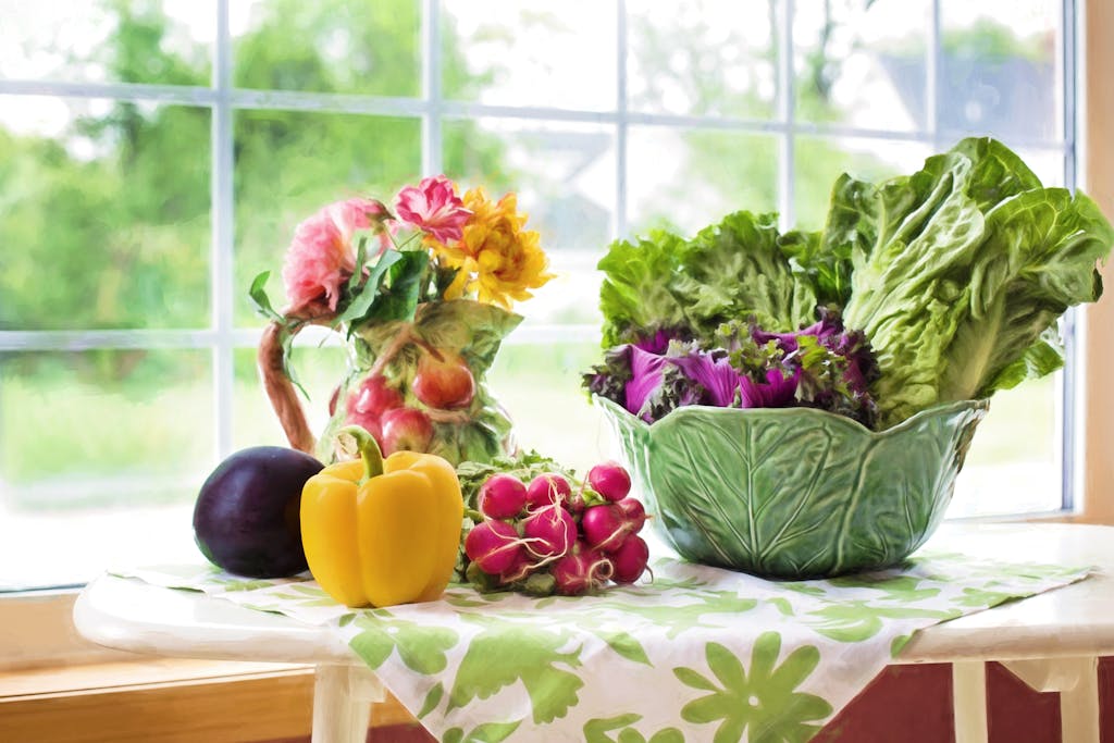 A vibrant display of fresh vegetables and flowers on a sunlit kitchen table by the window.
